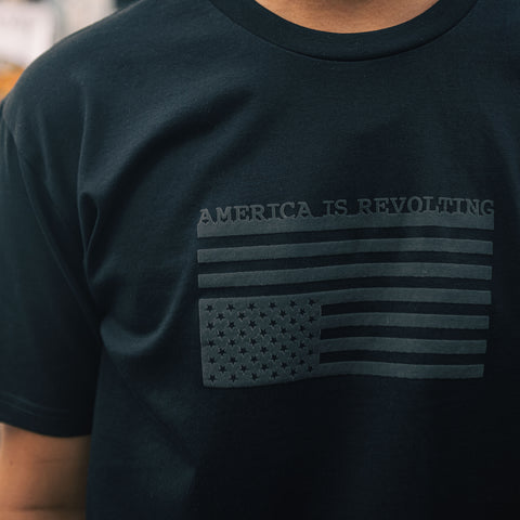 Black t-shirt with American flag graphic upside down and 'AMERICA IS REVOLTING' text in an off-black textured print