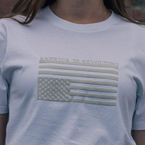White t-shirt with American flag graphic upside down and 'AMERICA IS REVOLTING' text in an off-white textured print